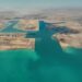 في إطار تنفيذ توجيهات فخامة الرئيس عبد الفتاح السيسي، رئيس الجمهورية، بالمضي قدمًا في خطة تطوير ورفع كفاءة الموانئ المصرية وتحويلها إلى مراكز إقليمية للنقل واللوجستيات وتجارة الترانزيت، يتواصل العمل بوتيرة متسارعة في مشروع تطوير ميناء السخنة، أحد أبرز الموانئ المصرية على البحر الأحمر. ويمثل ميناء السخنة أحد الركائز الأساسية لممر لوجستي عملاق يربط بين البحرين الأحمر والمتوسط عبر محور "السخنة – الإسكندرية"، في إطار المخطط المتكامل لتطوير موانئ الجمهورية وتعزيز قدراتها التنافسية على خريطة التجارة الإقليمية والدولية. وقد شهد المشروع إنجازًا هامًا بتسجيل نسبة تنفيذ 100% في أعمال البنية التحتية لمحطة حاويات "هاتشيسون"، أولى المحطات ضمن خطة تطوير الميناء، مع تواصل العمل في تنفيذ أعمال البنية الفوقية التي تشمل إنشاء الساحات، المباني الإدارية، والأسوار. ويمتد ميناء السخنة على مساحة 29 كيلومترًا مربعًا، ويتضمن المشروع إنشاء 5 أحواض جديدة و18 كيلومترًا من الأرصفة البحرية بعمق يصل إلى 18 مترًا، بالإضافة إلى ساحات تداول بمساحة 9.2 مليون متر مربع، ومناطق لوجستية بمساحة 5.2 كيلومتر مربع، إلى جانب شبكة طرق داخلية بطول 17 كيلومترًا من الرصف الخرساني، وشبكة سكك حديدية بطول 30 كيلومترًا متصلة بخط القطار الكهربائي السريع. ويُعد المشروع جزءًا من المخطط الشامل لتحويل ميناء السخنة إلى ميناء محوري متكامل، بما يسهم في مضاعفة حصة مصر من تجارة الترانزيت العالمية، وتعزيز تنافسية الموانئ المصرية كمراكز إقليمية وعالمية للخدمات اللوجستية. وفي هذا السياق، يأتي التعاون مع كبرى التحالفات العالمية في إدارة وتشغيل الخطوط الملاحية ومحطات الحاويات الدولية كخطوة استراتيجية ضمن خطة وزارة النقل لعقد شراكات مع أكبر الشركات المتخصصة عالميًا، بما يضمن جذب مزيد من الخطوط الملاحية وتكثيف حركة السفن بالموانئ المصرية، بما يواكب مستهدفات الدولة في تعزيز مكانتها كمركز إقليمي ودولي للتجارة البحرية والخدمات اللوجستية.